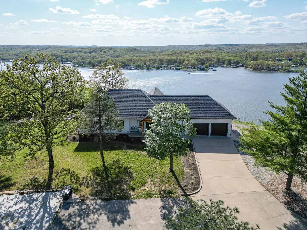 A wide shot of the house’s front yard overlooking the lake, featuring a spacious lawn, the house structure, and clear water views. The setting invites boating, picnicking, and enjoying the natural surroundings, with the house acting as a welcoming home base.