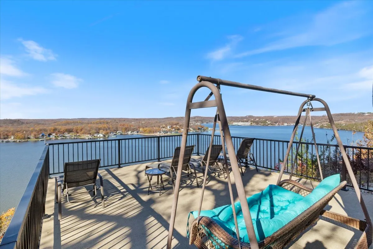 A tranquil balcony scene with a swing chair and lounge chairs facing a breathtaking water view, framed by a balcony railing. The setting exudes relaxation with options for reading, socializing, or simply soaking in the lake’s beauty at sunset or sunrise.