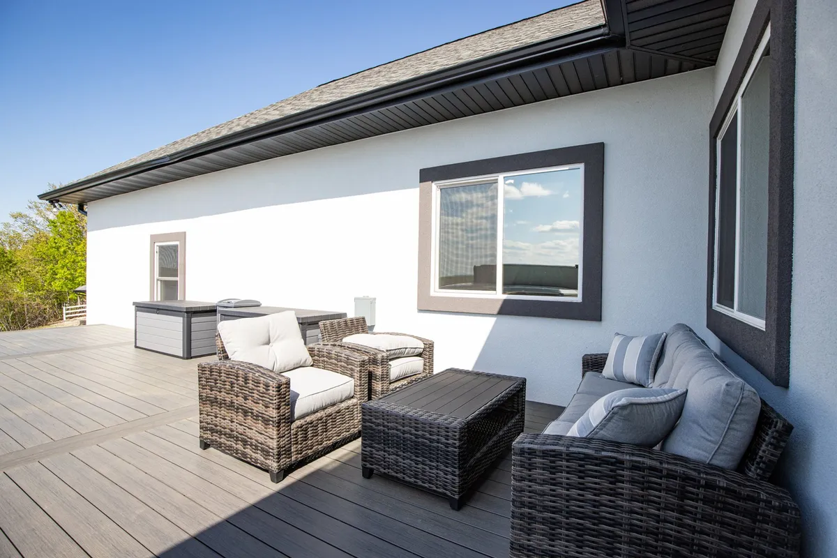 A spacious outdoor deck furnished with wicker seating and large windows connecting the deck to the indoors. The setting is ideal for gathering with friends, enjoying drinks, or simply relaxing while watching the sunset over the lake.