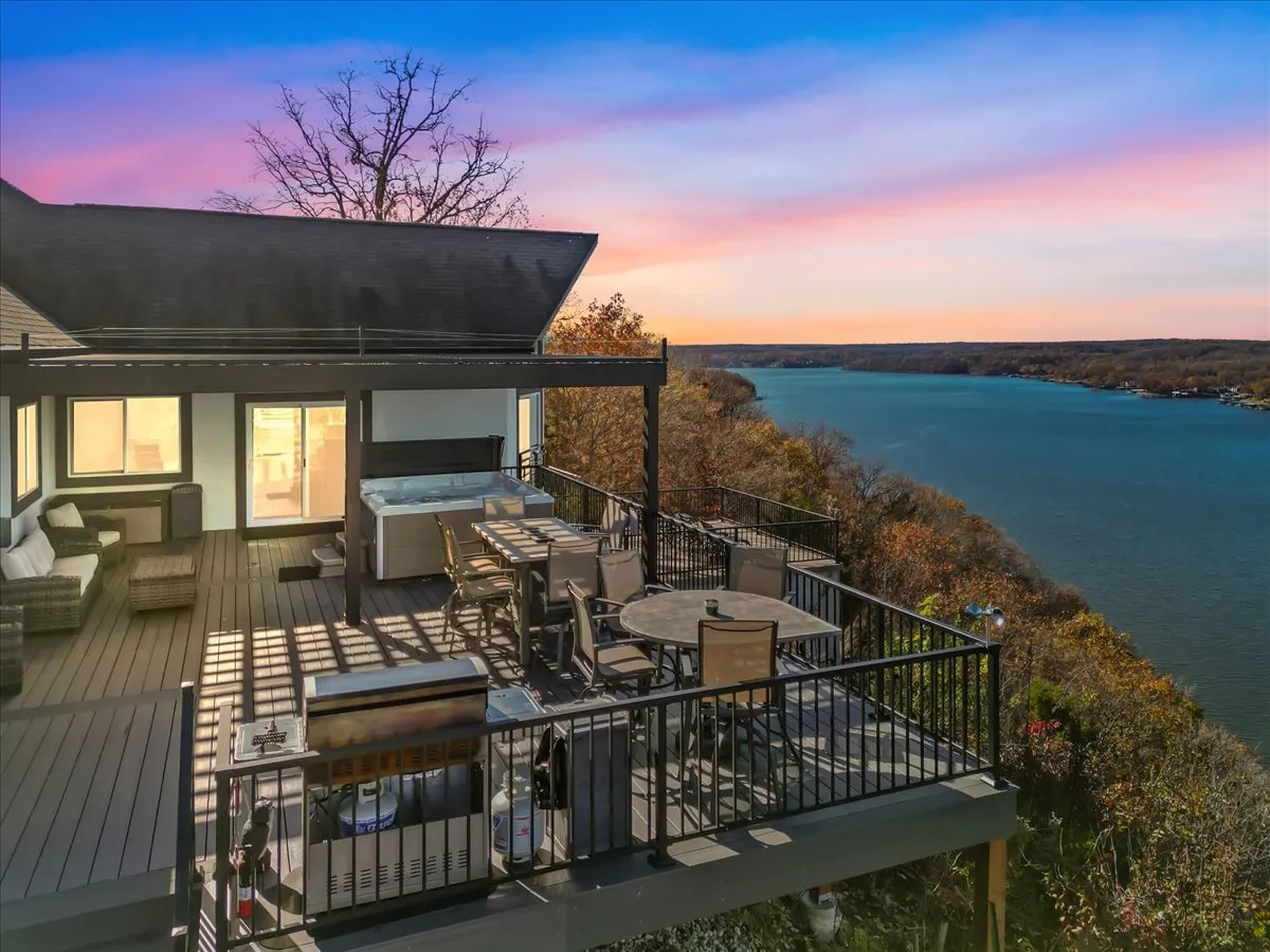 This image features an expansive deck with multiple seating options, a hot tub, and a sweeping river view. Lounge chairs and a dining table are arranged to take advantage of the scenic outdoors, while the hot tub is prominently placed for relaxation with a view.