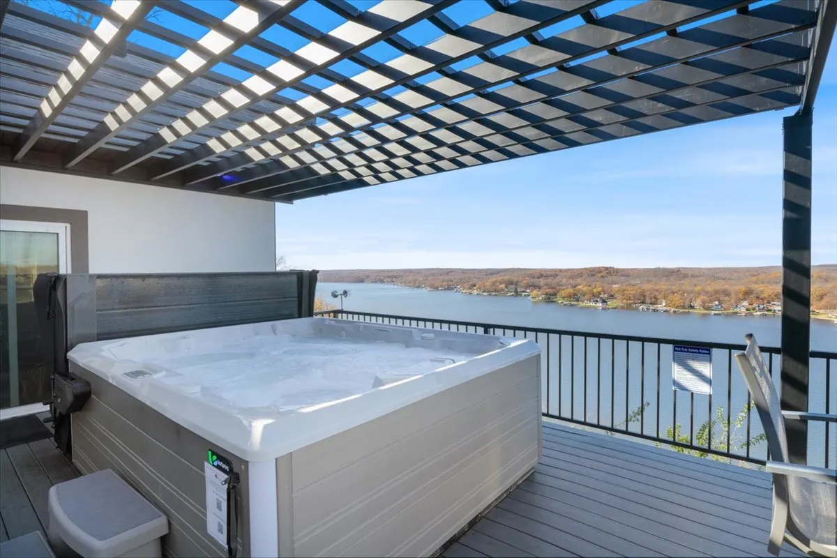 This exterior shot features a hot tub under a pergola overlooking a serene lake. The setup invites guests to relax while taking in stunning sunset views, with a clear connection to the water and natural surroundings.