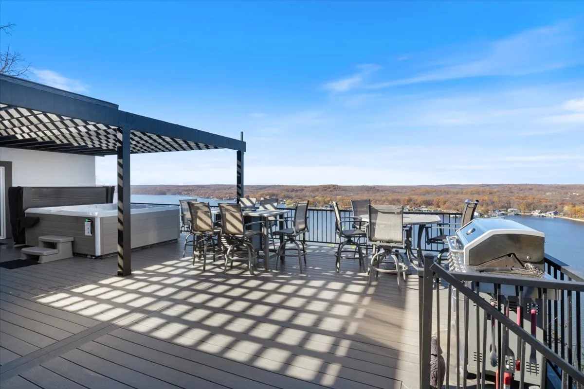 A vibrant exterior shot showing a hot tub, outdoor dining set, grill, and a wide-open view of the water. The grill and dining table are ready for an alfresco meal, while the hot tub sits nearby, offering relaxation with an unmatched lakeside backdrop.