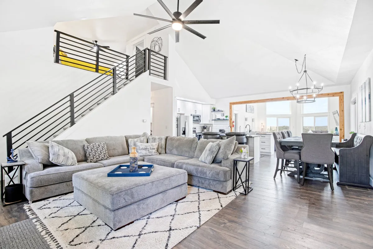 This image showcases an expansive interior featuring a large sectional sofa, a dining table, and an open kitchen, all bathed in natural light streaming through generous windows. The space is clearly open-concept, allowing seamless flow between living, dining, and cooking areas, with modern décor and comfortable seating.