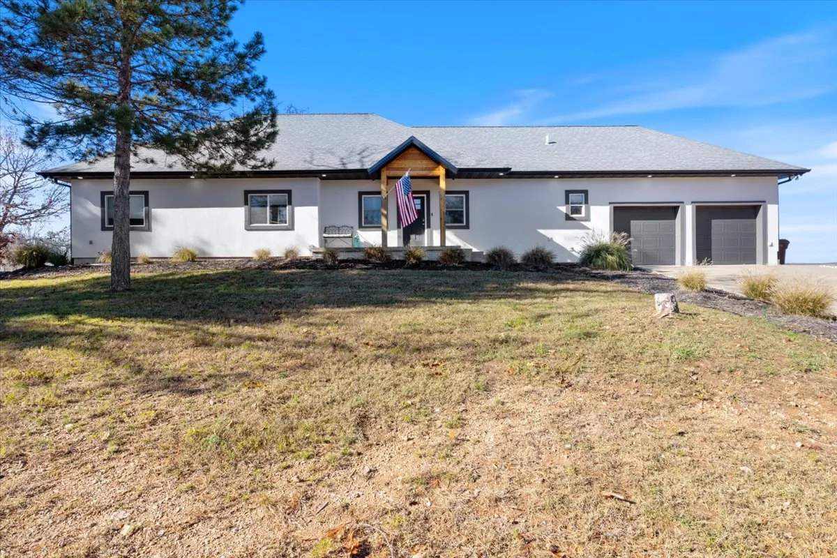 This exterior image features the front entrance of the home, flanked by a landscaped yard and garage doors, with an inviting porch and an American flag. The setting conveys a welcoming and secure arrival experience.